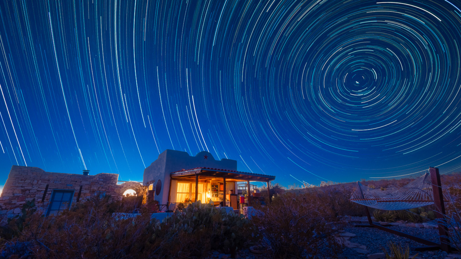 Star trails over a desert cabin.