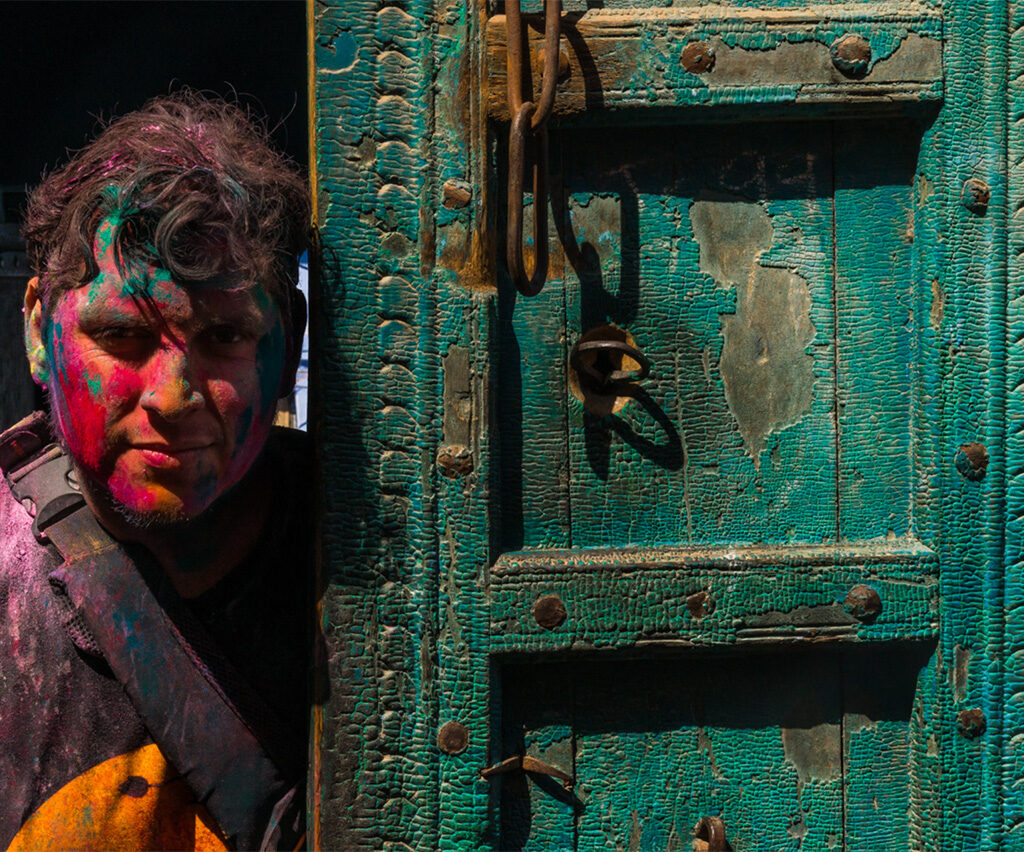 A powdered-color-coated figure standing next to an old green door.
